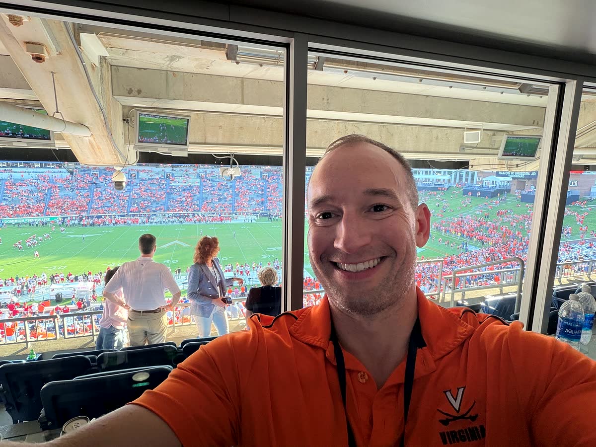 Selfie from inside the box at Scott Stadium, with the field and the crowd visible through the glass.