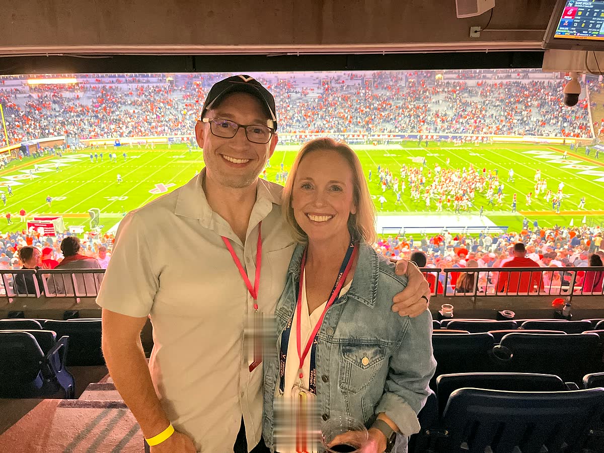 Ben and Nicole in the president's box at Scott Stadium, a packed night crowd and the field behind them.