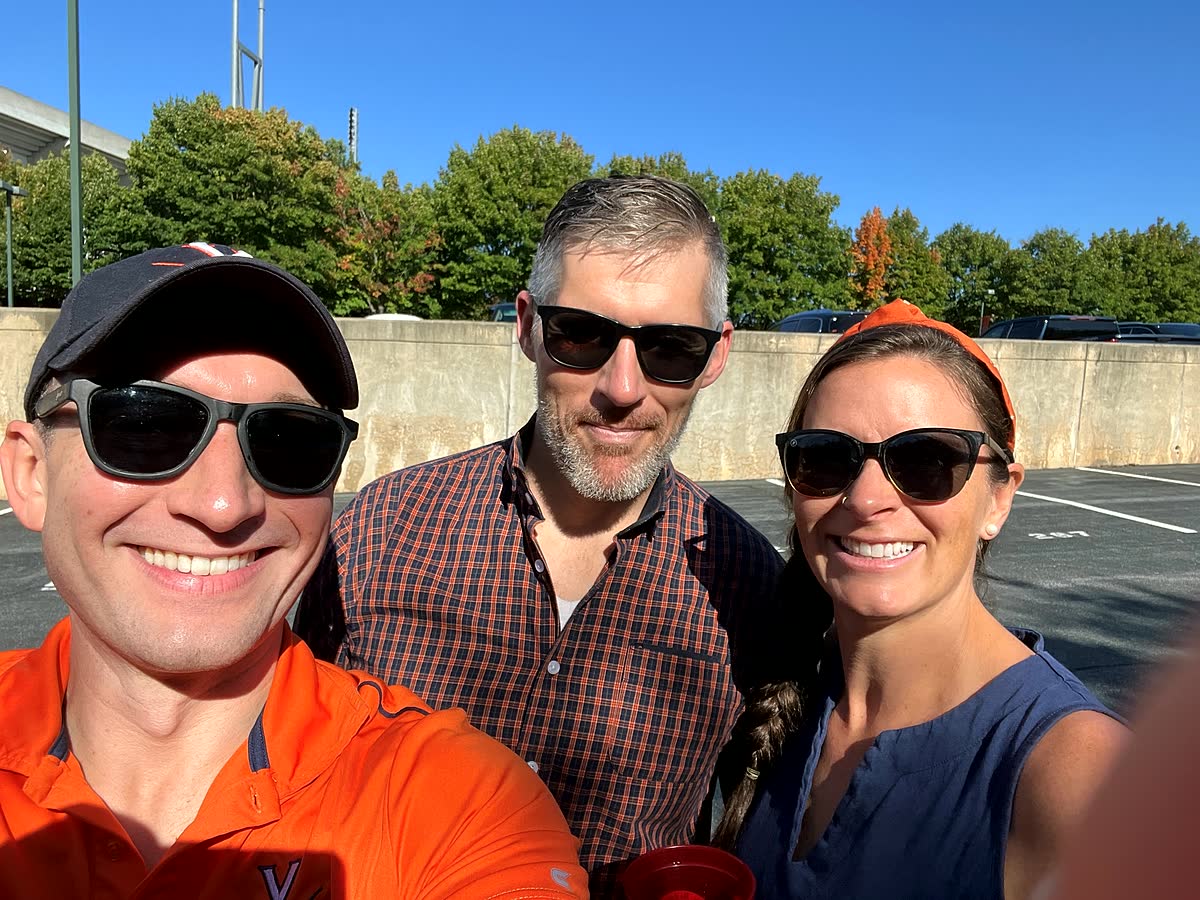 Three of us in sunglasses in the Scott Stadium parking lot under a bright blue sky.