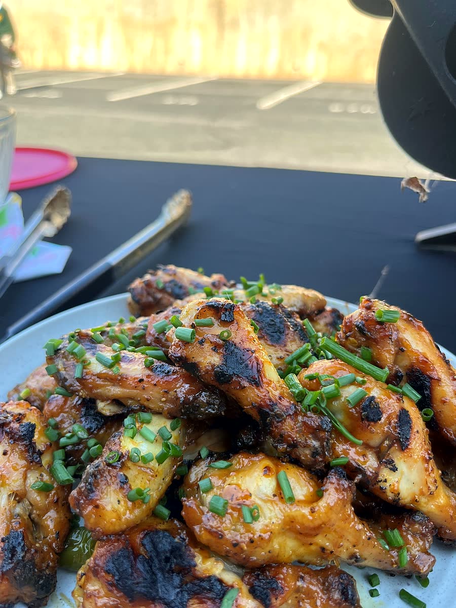 A plate of charred grilled chicken wings covered in chopped chives on a tailgate table.